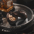 A tray with a iron football box with thee lid on its side, inside are pistachios. Behind it is a  bottle.