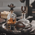 A tray with two decanters with iron toppers, a iron football and two dark shot glasses. 