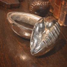 A nickel plated football ball box with a open lid resting on its side. On a wood surface.