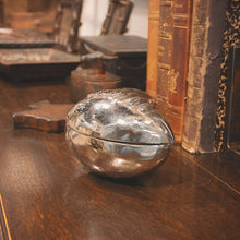 A nickel plated football box on a woo surface and some old books.