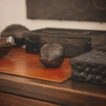 A iron baseball on top of a orange leather mat, surrounded by iron boxes.