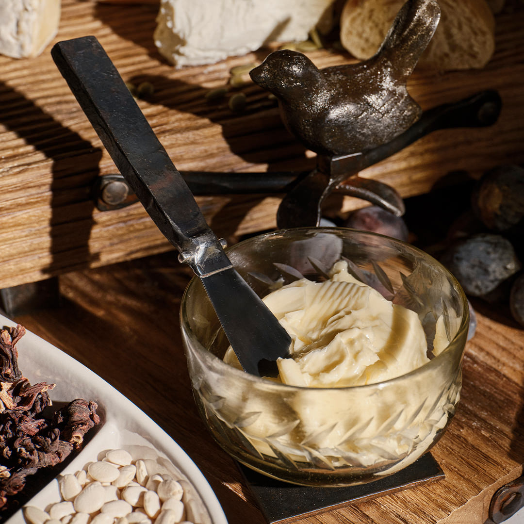 A iron bird and a glass bowl with a cream inside. A stainless steel knife with forged handle is stuck in the cream. Wooden background.