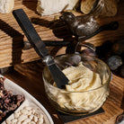 A iron bird and a glass bowl with a cream inside. A stainless steel knife with forged handle is stuck in the cream. Wooden background.