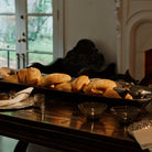A hand-carved hammered long bowl w/ five cast birds filled with bread on top of a table wit some glasses.