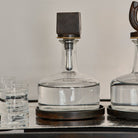 A iron squared top decanter and leather lined iron tray In  the middle of another decanter and two glasses with liquid.