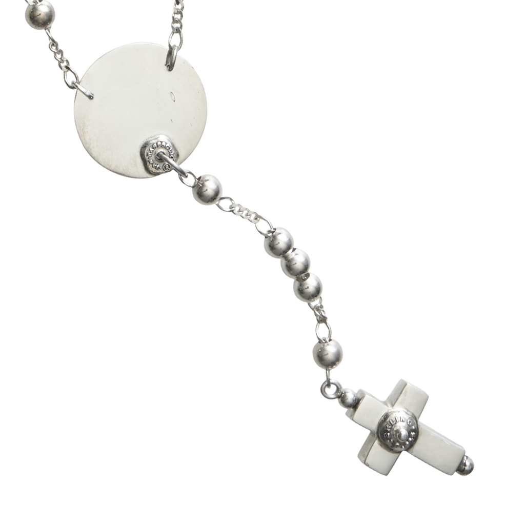 A delicate silver necklace  with a fine chain design and a circle near the end with a cross charm in the end, displayed on a plain background.