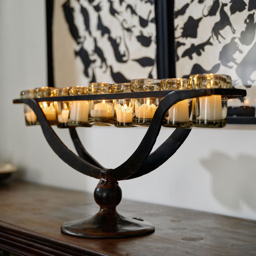 A nine votive holders with lit candles supported by  forged iron outstretched arms.  On the background is a black and white frame.