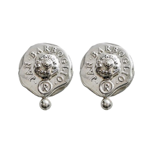 Silver earrings with a seal. The seals says thee name of the designer and place of origin. A small silver bead in under the seal.