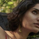 Part of a woman face. She is looking up. She is wearing a bronze hook earring. The bottom of the earring has a half circle or open fan shape. The earring has two seals. The earring is a the center of the picture.