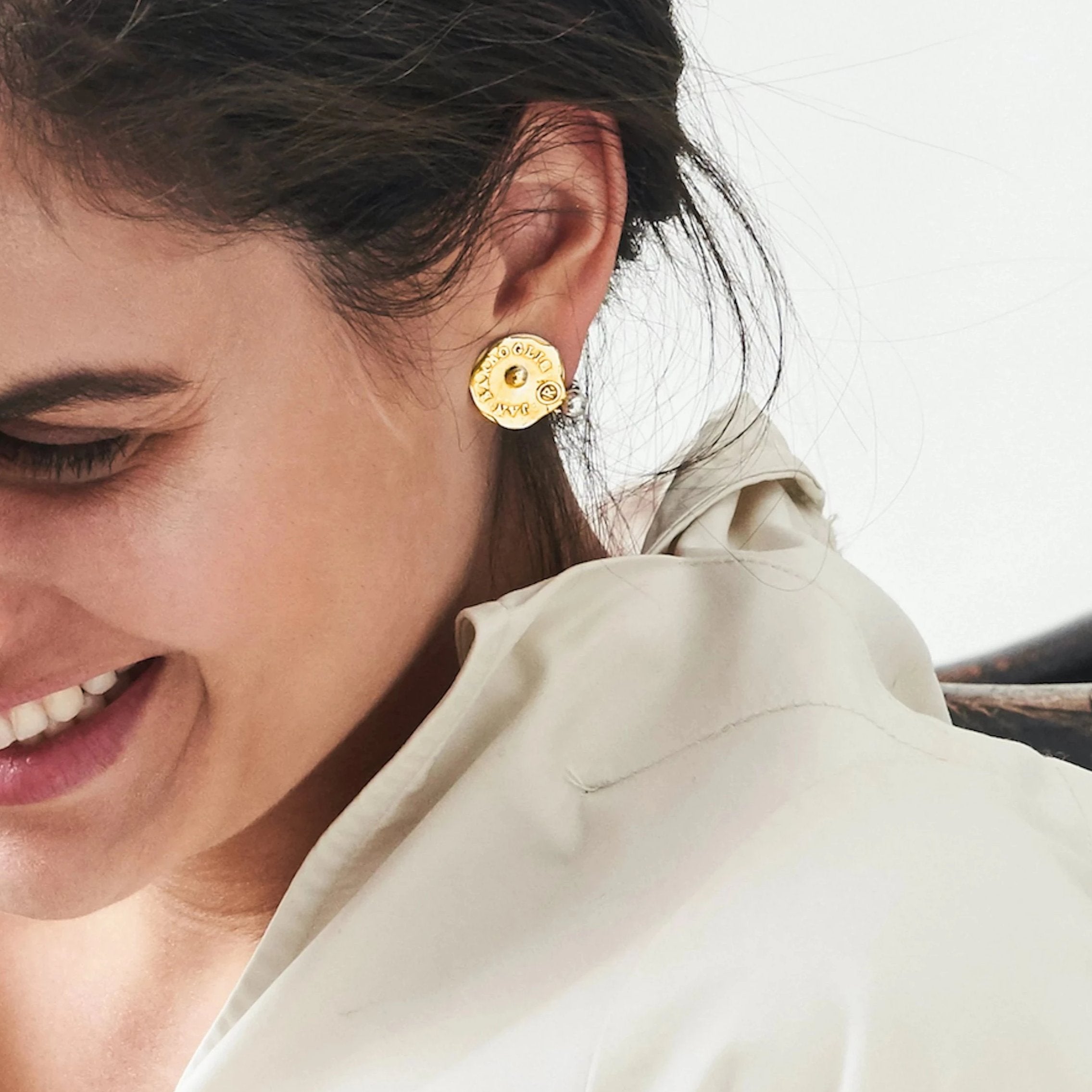 A woman laughing. She is wearing a circular gold earring with a silver ball.