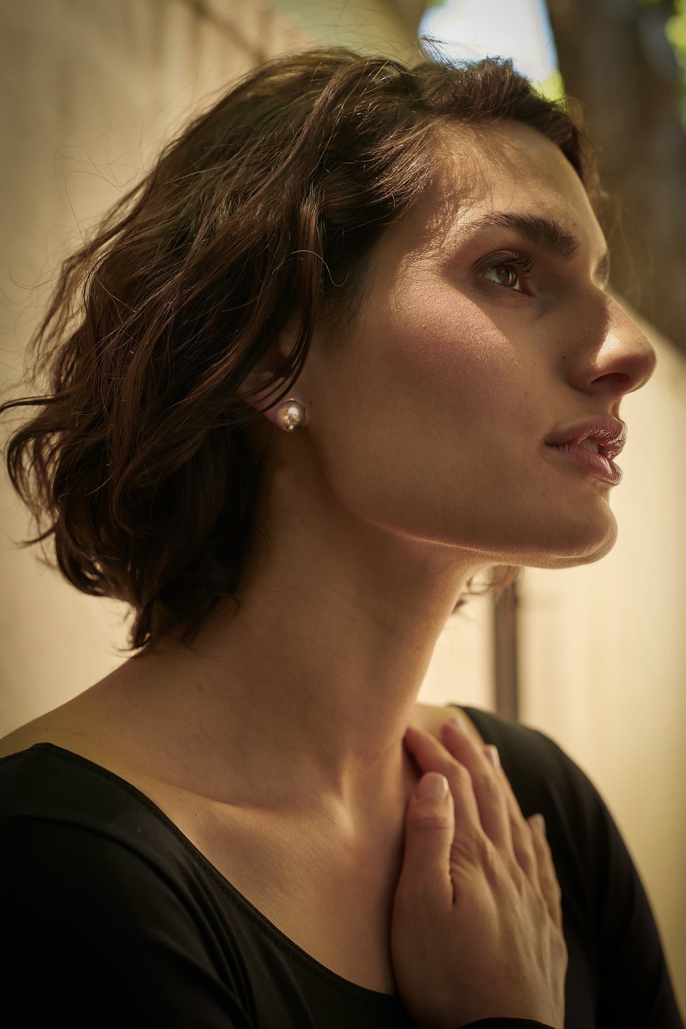 A woman's profile wearing a bronze stud in her ear. She is wearing black and outside.