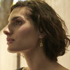 A profile of a woman wearing golden  hook earring holding an egg shaped sculpture with two seals.