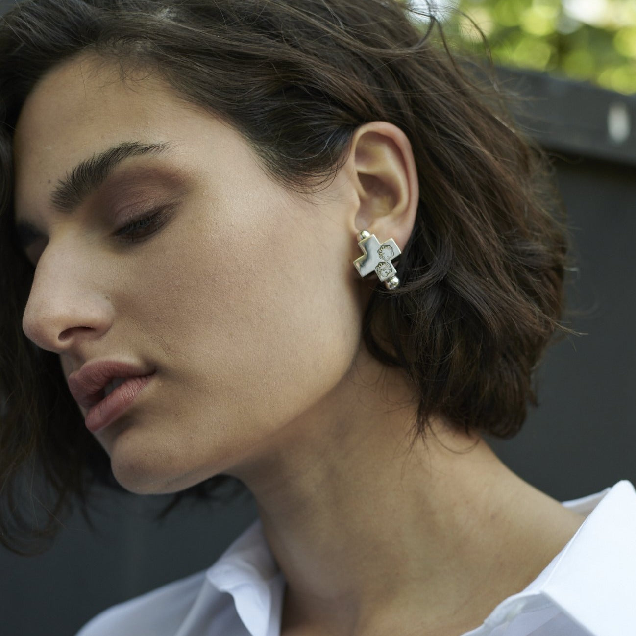 The face of a woman. She has short hair and is wearing silver cross earrings.