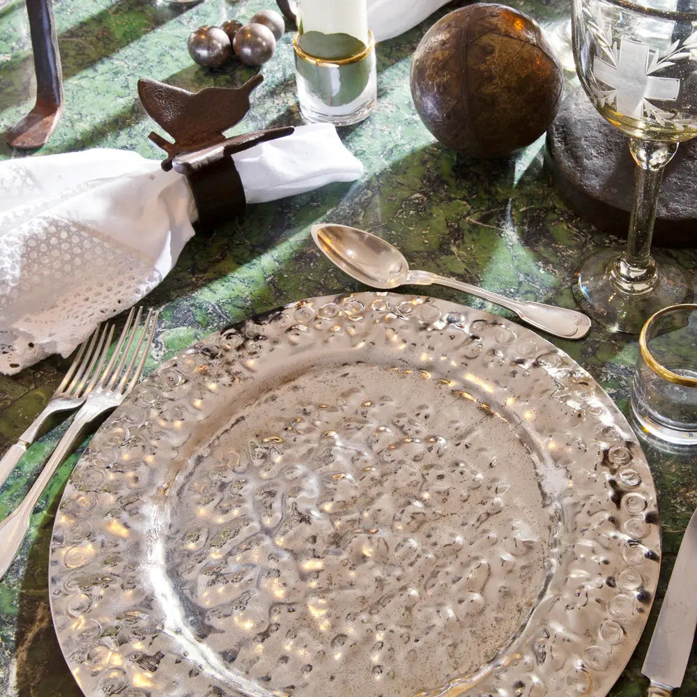 A green surface with a nickel plate, two forks and a spoon. Some cups and fabric napkins.