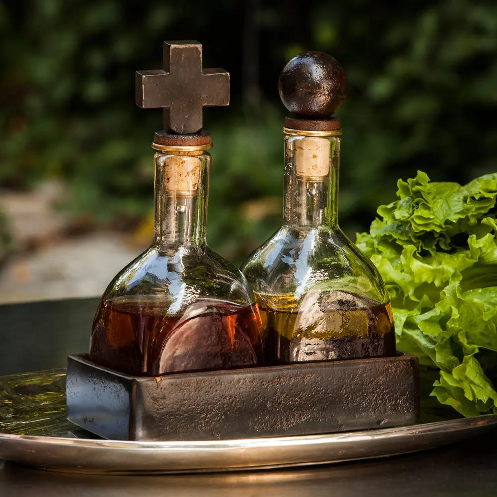 Twin glass bottles with  a ball and cross iron toppers in wax cast iron coaster. Both bottles are filled with liquids. Outside background.