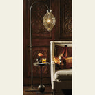 A  hanging lamp. under the lamp is a table with a iron stand and a rose and a glass. Next to it is a sofa. The background is a carved wood.