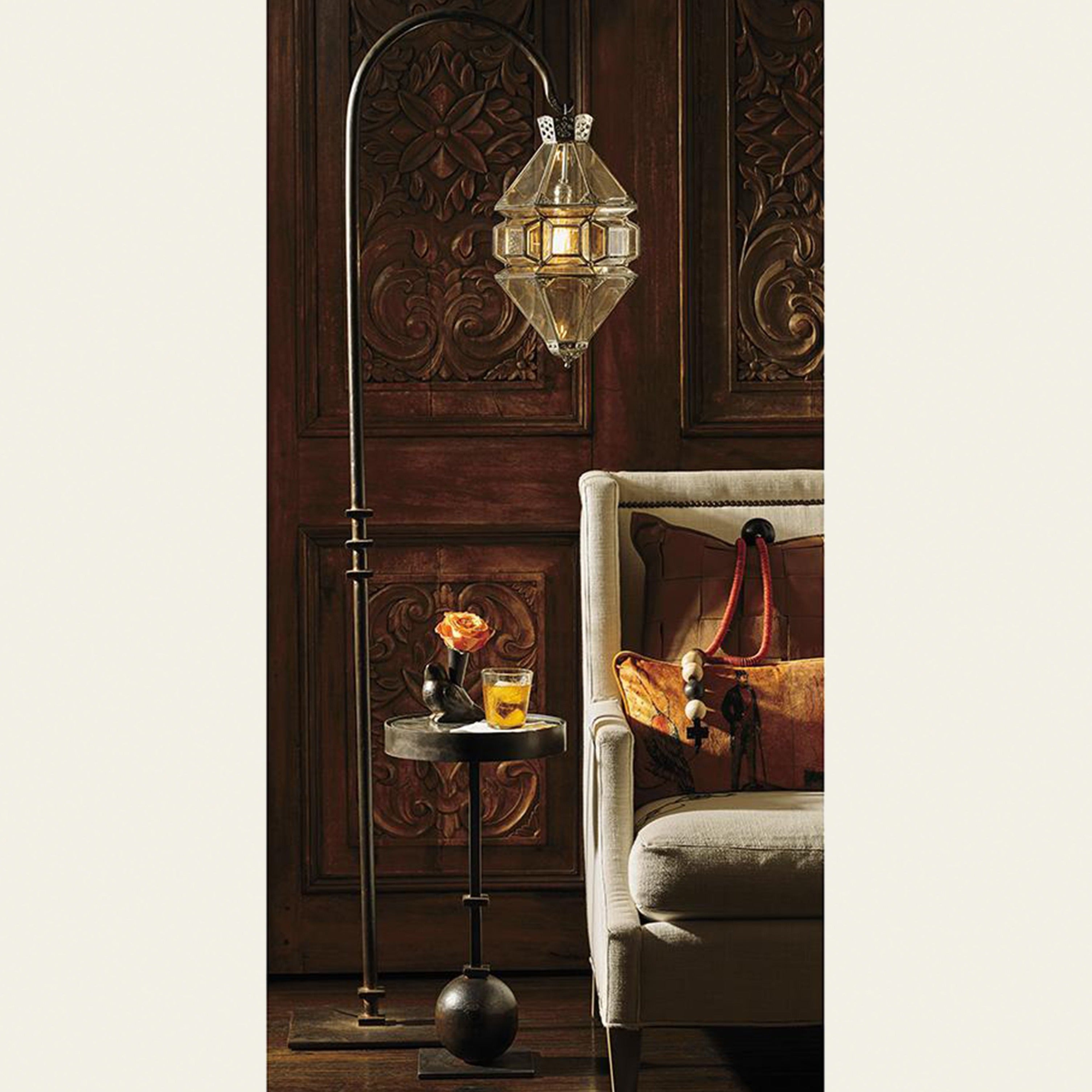 A  hanging lamp. under the lamp is a table with a iron stand and a rose and a glass. Next to it is a sofa. The background is a carved wood.