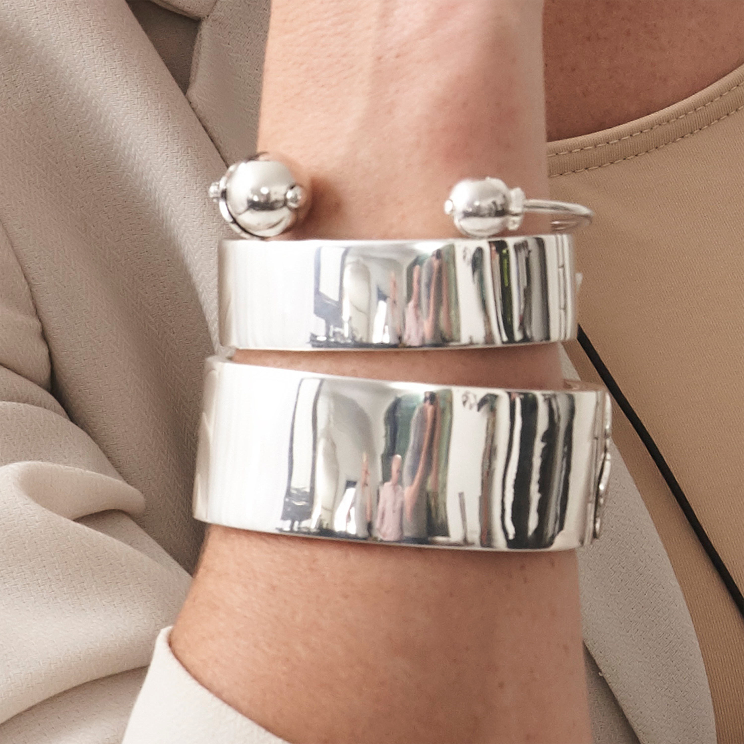 A wrist with three silver bracelets. One is simple with two beads, the other two and plain ones, one bigger then the other.