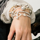 Wrist  resting in a wooden surface with silver bracelets. Most of the bracelets have silver beads.