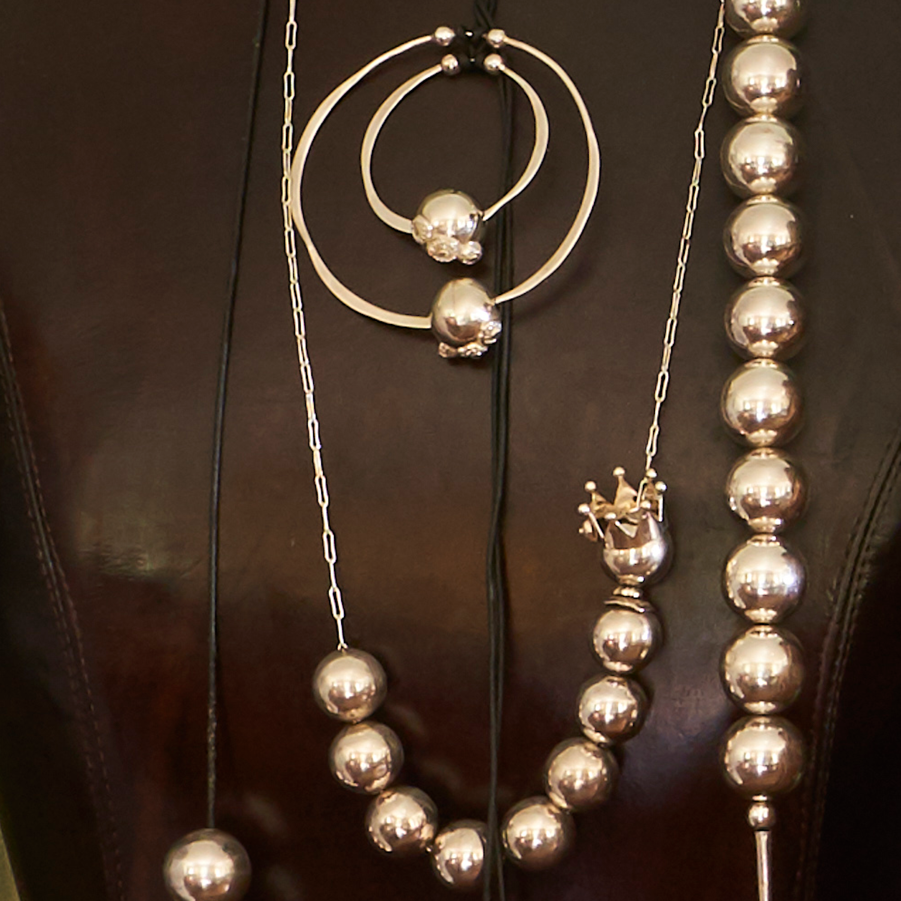 Several silver necklace with beads and hoops resting on a leather background.