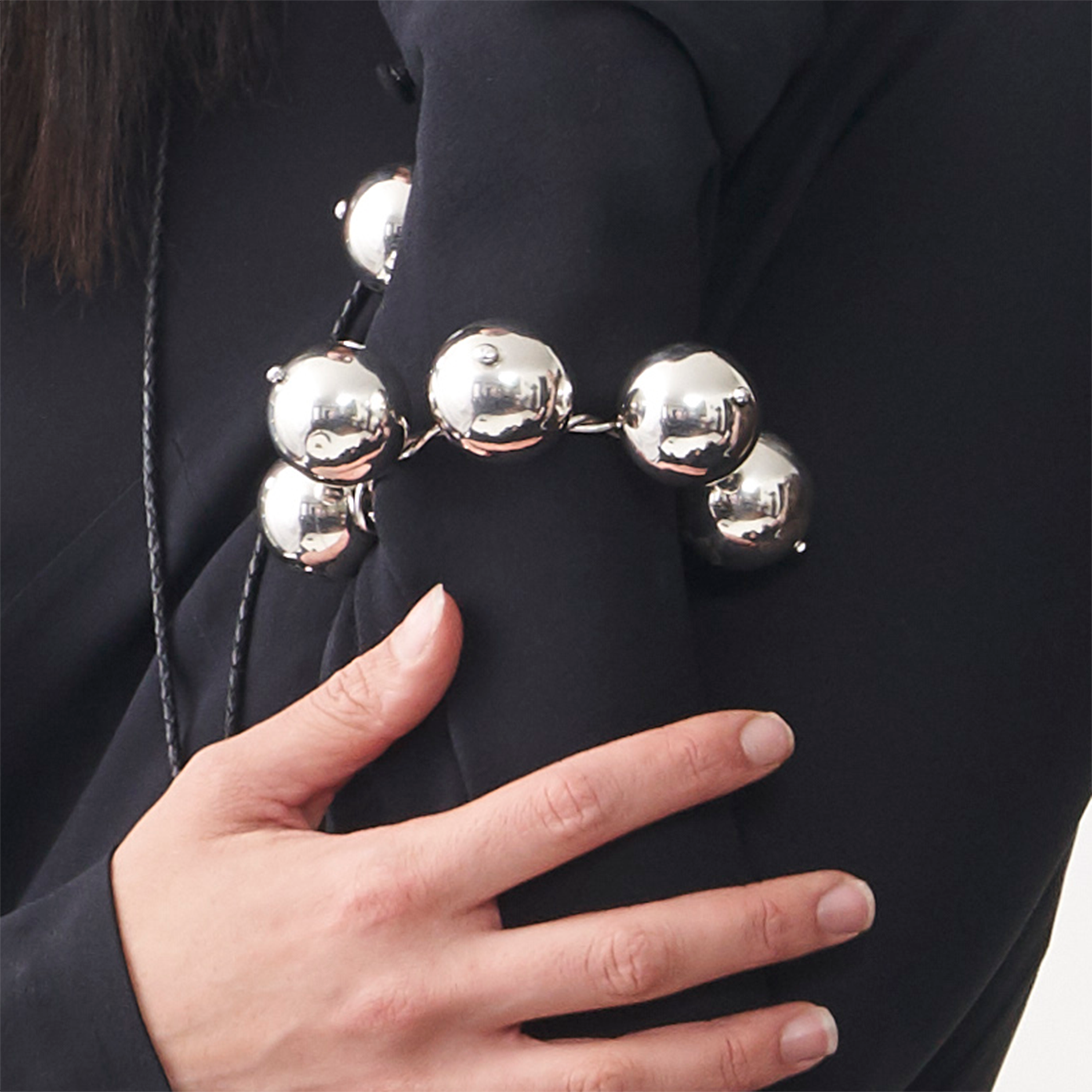 A silver bracelet with big silver beads around it resting in a black surface. A woman's hand is in the picture.