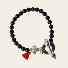 A black bead bracelet with a red string charm and a silver cross charm. Plain background.