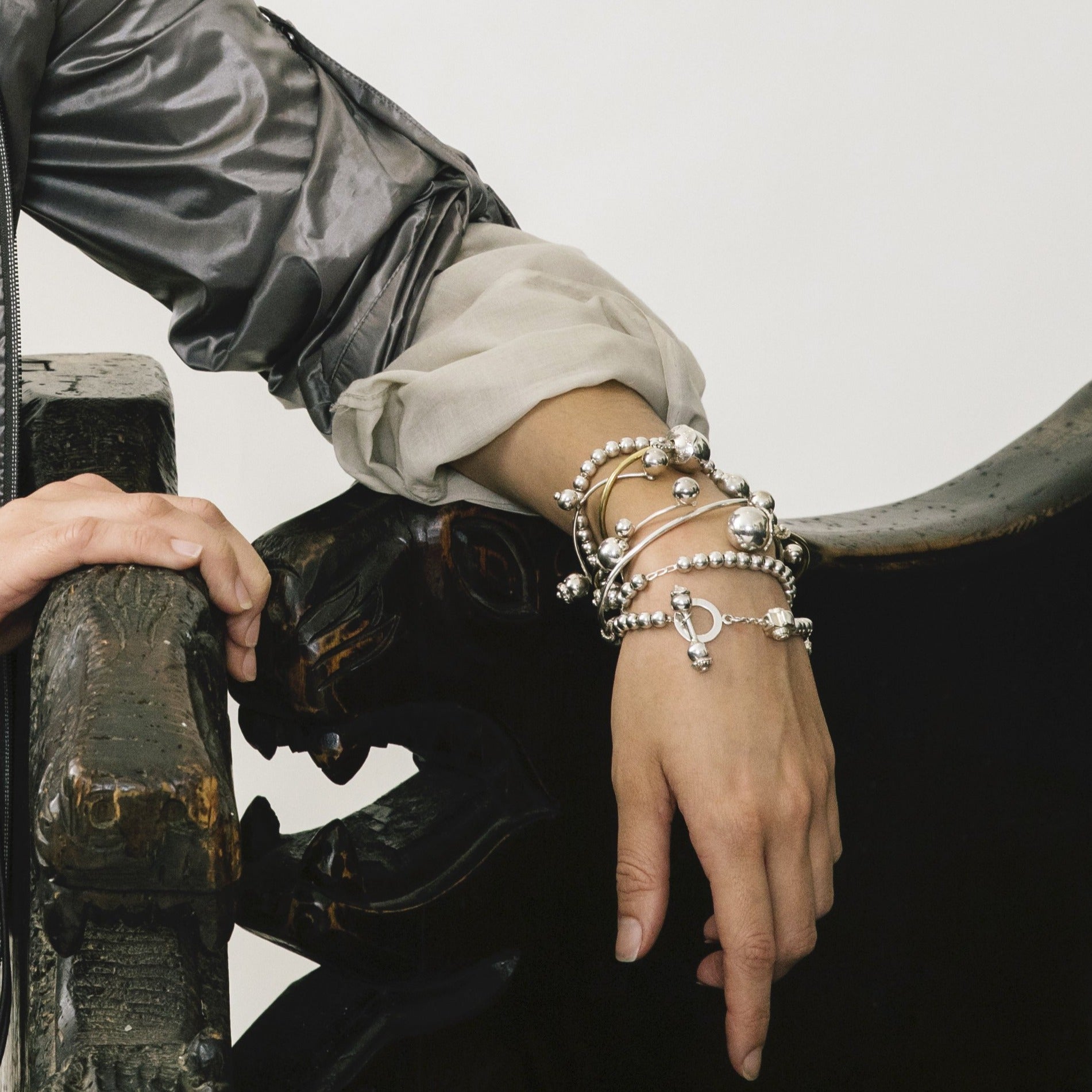 A woman's hand resting on a chair. She is wearing several silver beads bracelets.