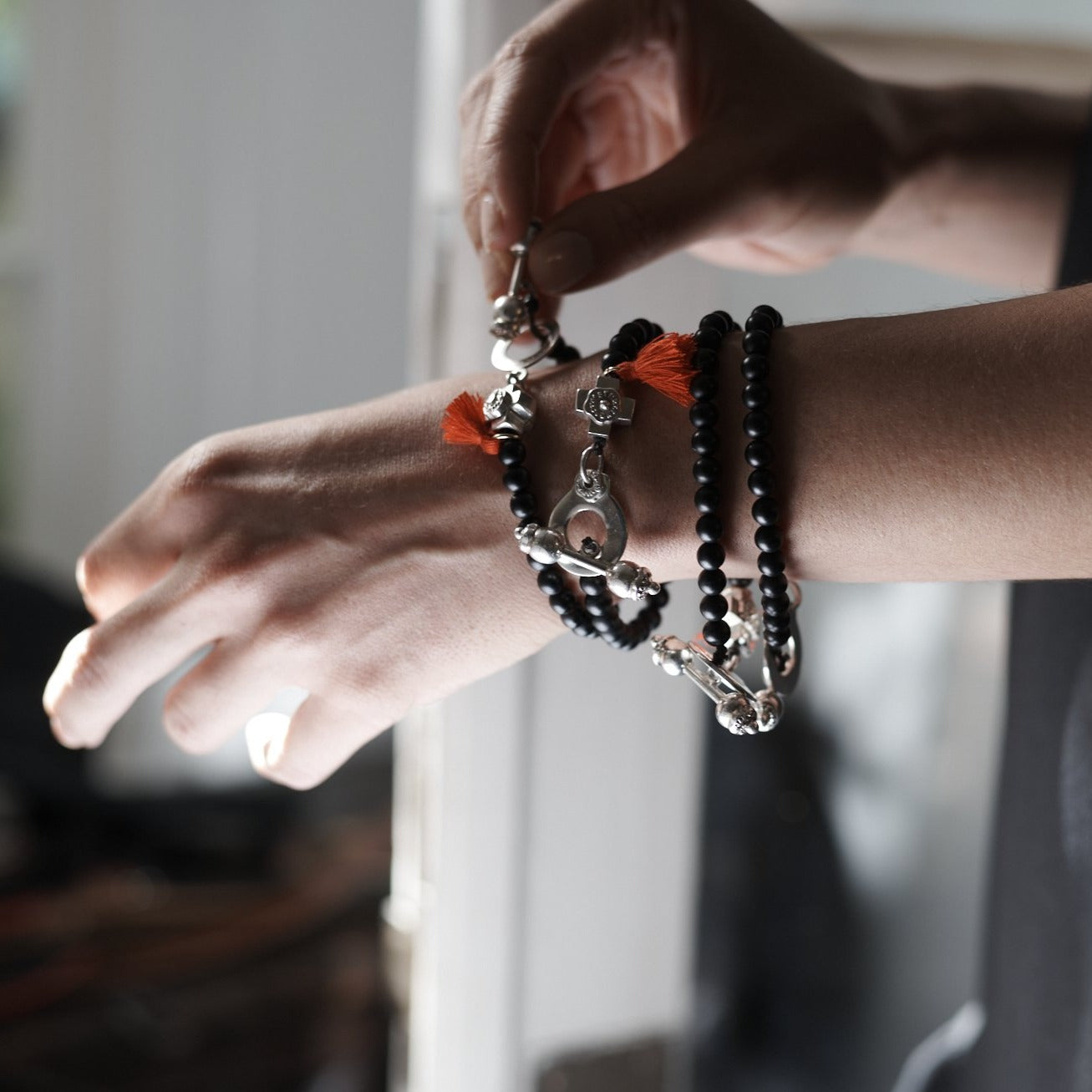 A woman's wrist with several black bead bracelets with a cross and red string charm.