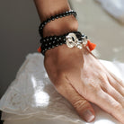 A woman's hand pressing down. In her wrists are several black beads bracelets with a silver closing system.