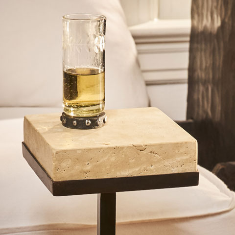 A glass with a yellow liquid on top of a stone table with an iron stand. In the background is part of a white sofa.