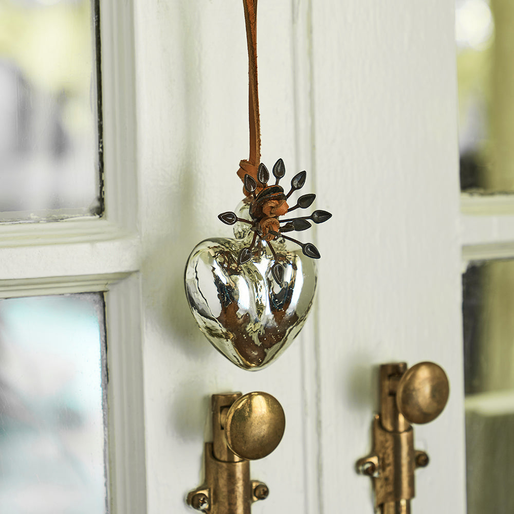 A blown glass heart with platinum finish on leather cord hanging from a door.