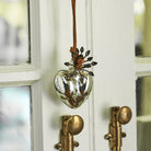 A blown glass heart with platinum finish on leather cord hanging from a door.
