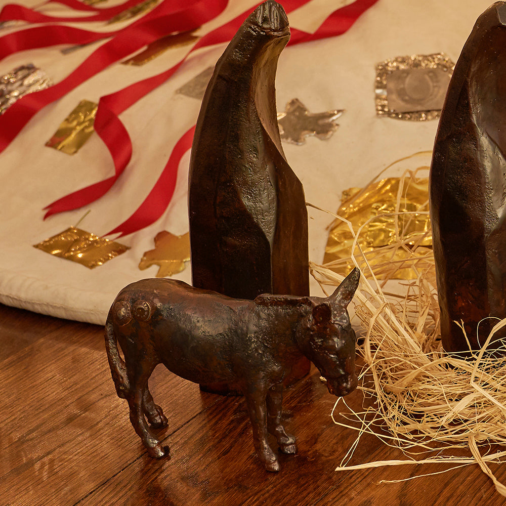 One iron donkey and two  other iron figurines. Some rafta and behind a white cloth with red ribbons and golden and silver figurines.