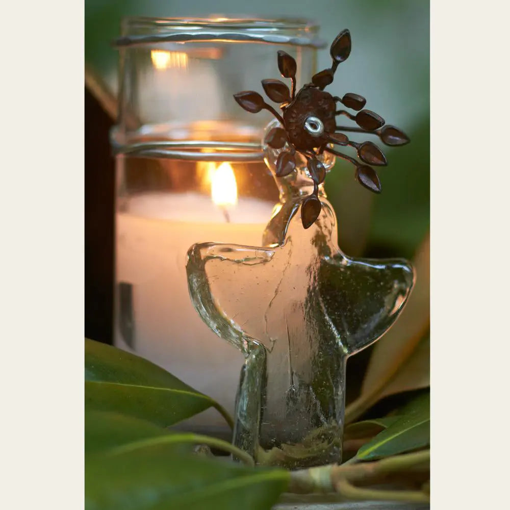 Poured candle in glass votive with mouth blown angel. Some green leaves on front.