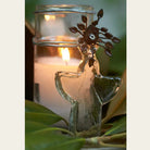 Poured candle in glass votive with mouth blown angel. Some green leaves on front.