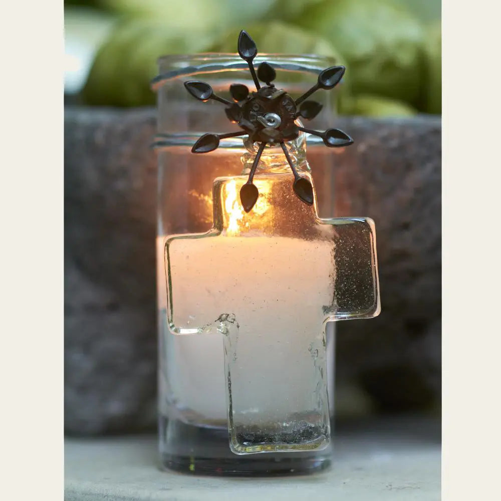 A poured candle in glass votive with mouth blown house blessing cross, iron flower. Outside background.