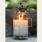 A poured candle in glass votive with mouth blown house blessing cross, iron flower. Outside background.