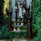 Several  angels with praying hands. Two have a lit candle on top. Several lit glass candles on stairs. Everything is in a garden.