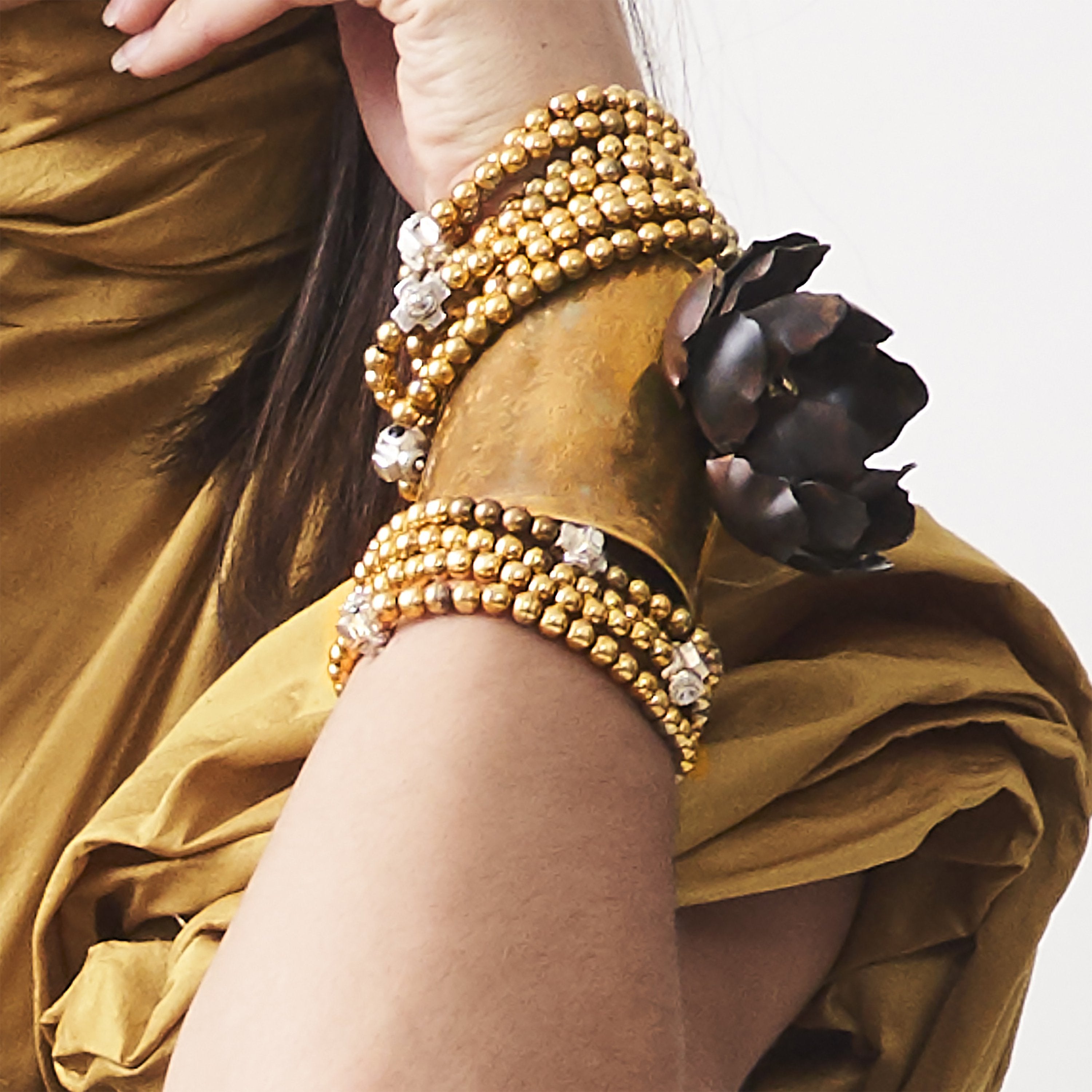 A woman's wrist with several bronze beads bracelet and a cuff with a dark metal rose.