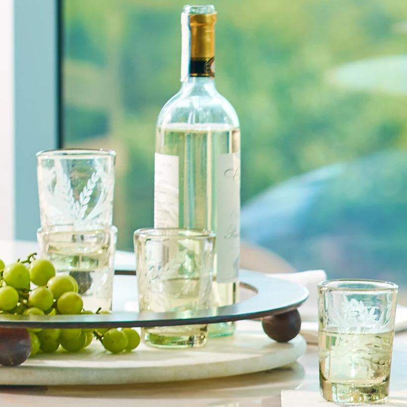 A tray with grapes, three glasses and a white wine bottle.  A glass with wine is outside of the tray.