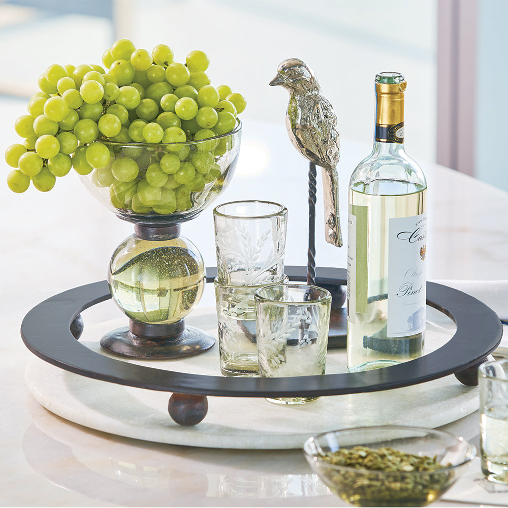 A tray with a bowl with grapes, a nickel plated bird, three glasses and a white wine bottle.