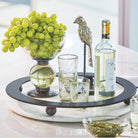 A tray with a bowl with grapes, a nickel plated bird, three glasses and a white wine bottle.