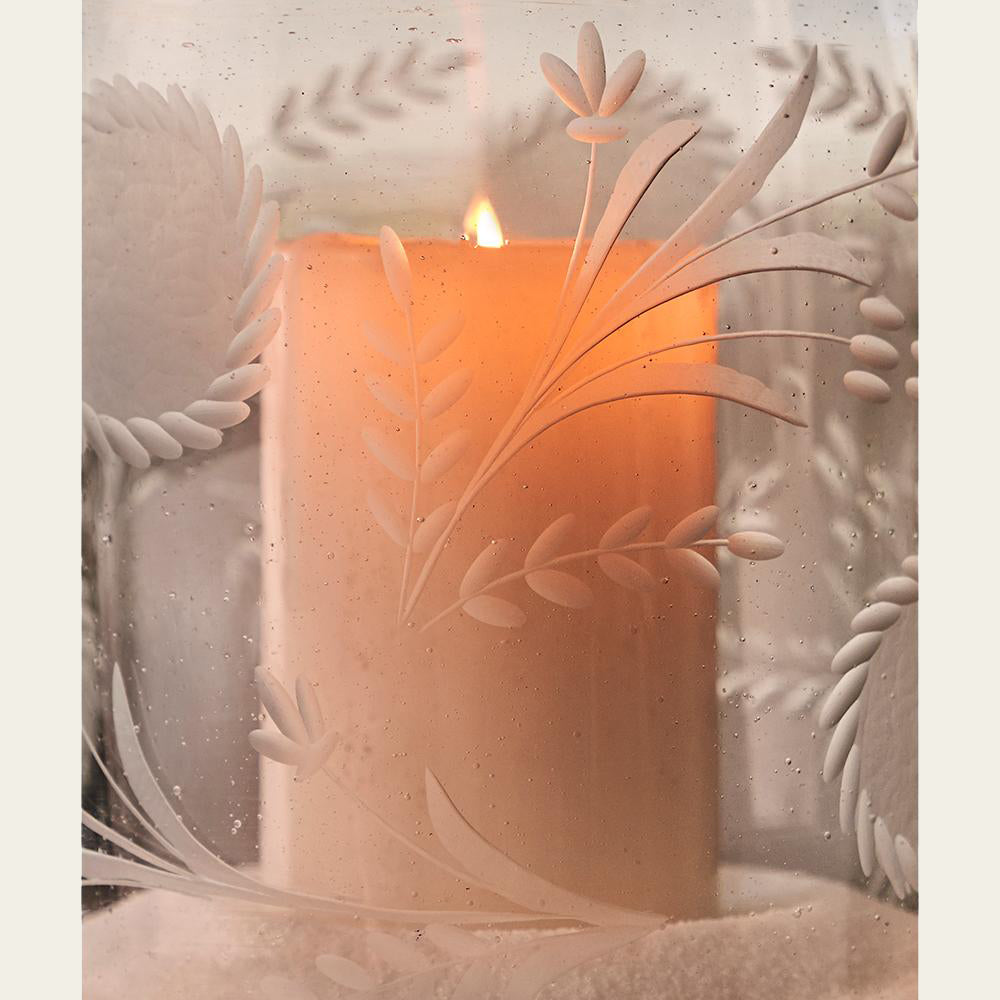 A lit candle inside a glass with engravings.