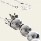 A silver crown with two seals followed by three silver balls. Plain background.