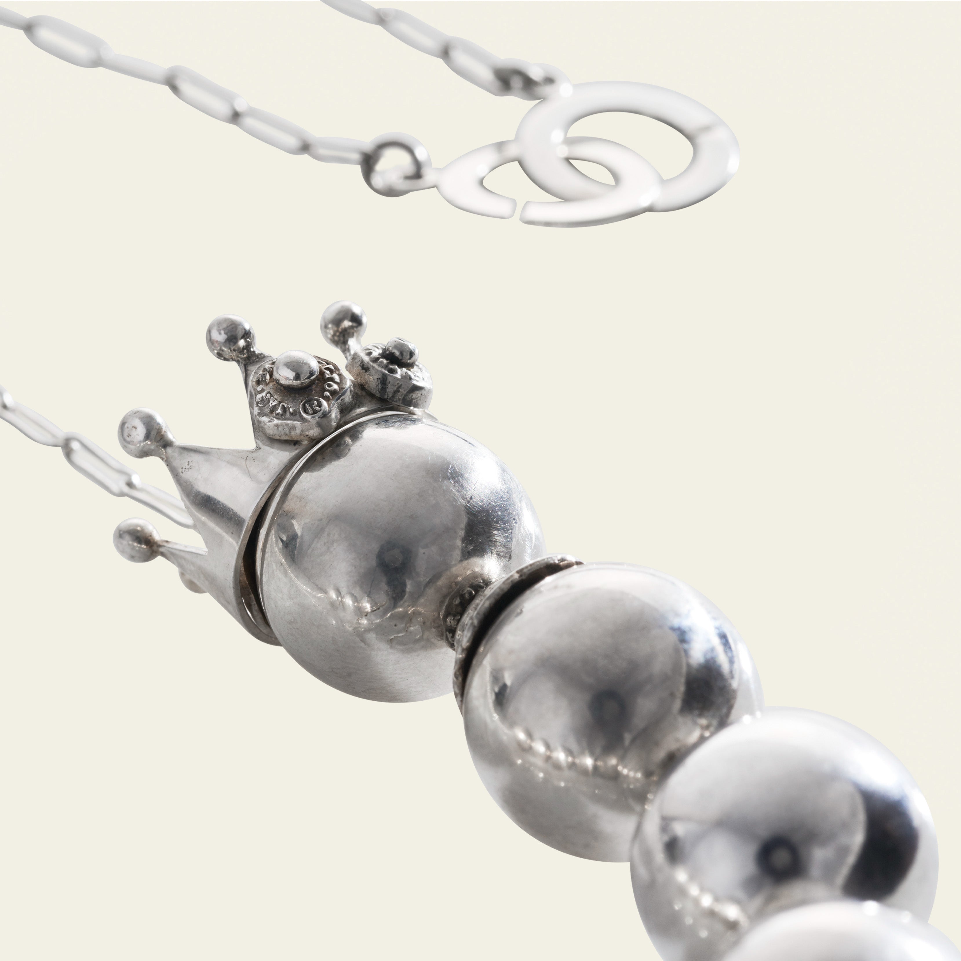 A silver crown with two seals followed by three silver balls. Plain background.