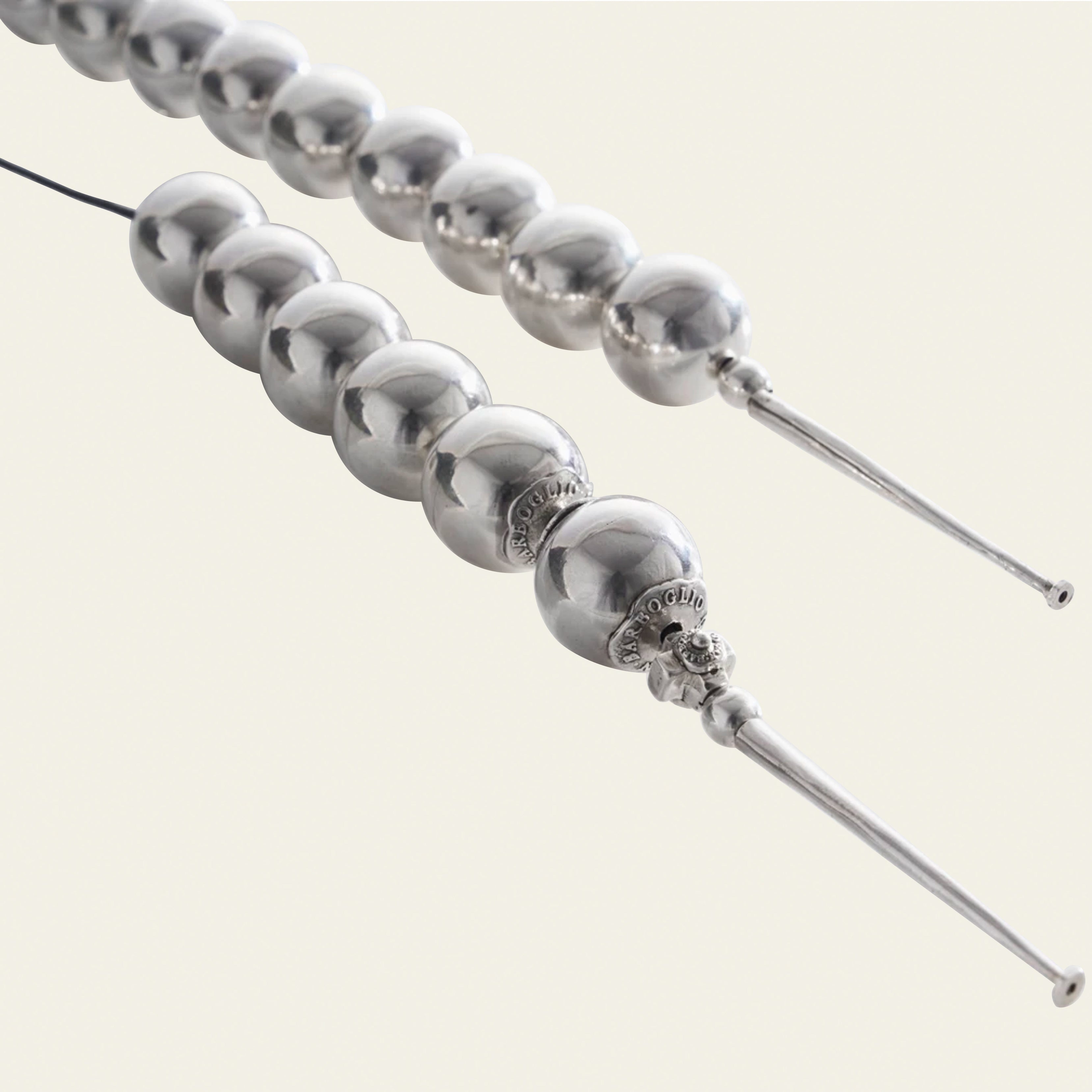 Silver beads with a cross charm and a silver stick. Plain simple background.