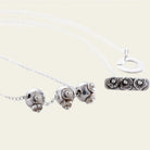 A delicate silver chain necklace with three ornate spherical charms featuring intricate designs. Alongside a rectangular charm engraved with seals featuring the brand logo.