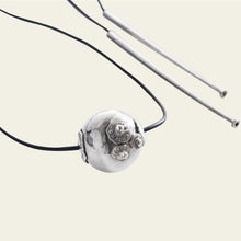 A silver bead with three seals engraved. The silver bead is hold by aa black leather string. In the right are two silver pieces.