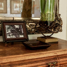 A wood furniture with a picture frame, a iron tray and a iron vase holding a glass with green leaves and seeds.