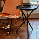 A brown chair next to a tripod  table with a bowl . On the background is a window.